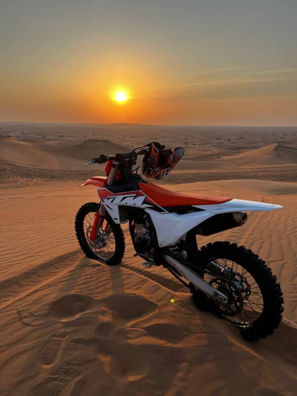 KTM Dirt bike aparcada en una duna del desierto de Dubai al atardecer
