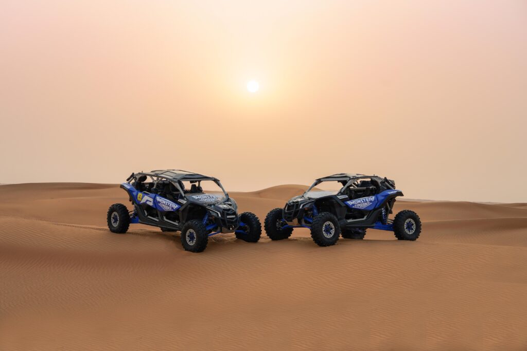 Two Monster Experience branded dune buggy's parked in the Dubai desert at sunset