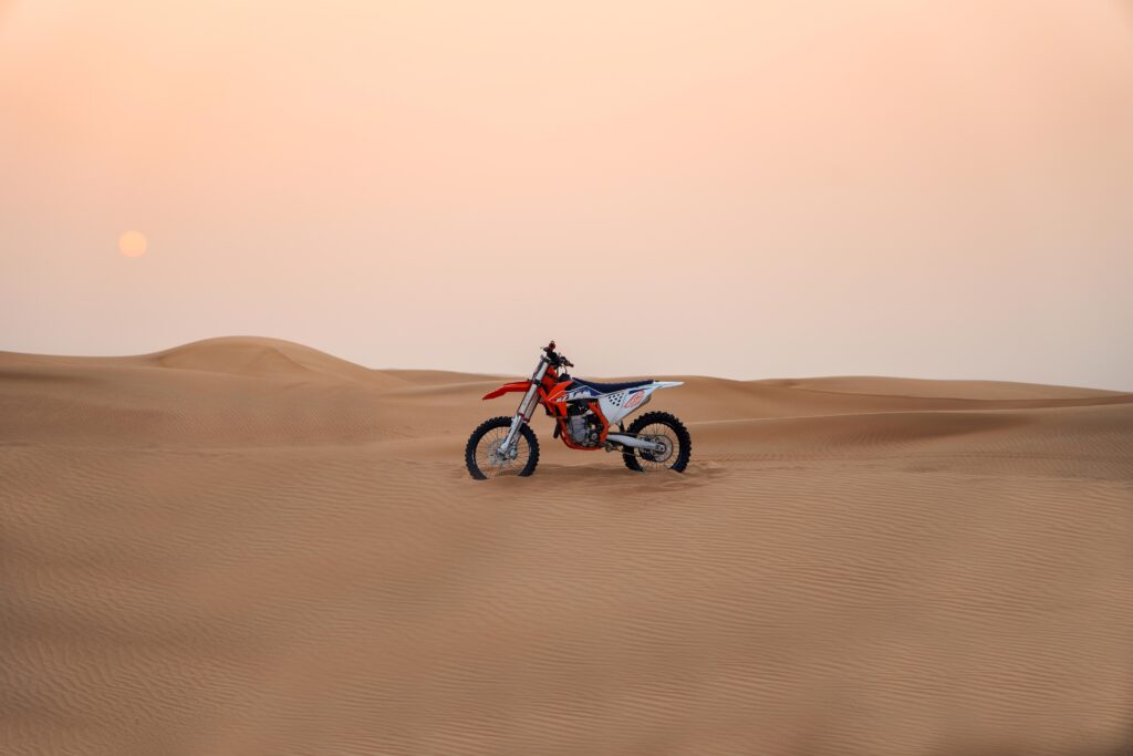 KTM motocross bike parked in the Dubai desert sand with sun setting in background