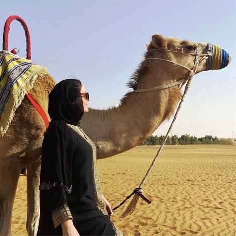 A female in abaya with camel in the desert