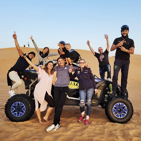 a bunch of friends having fun in the desert posing for camera standing around buggy