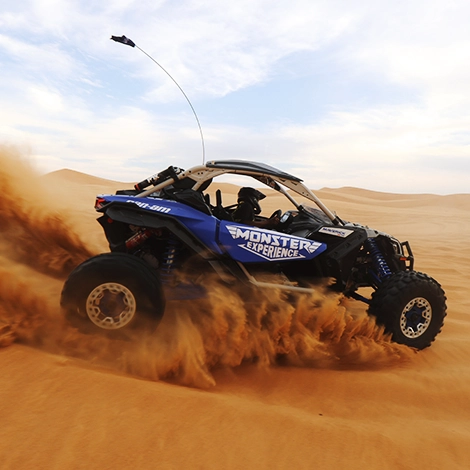 a blue buggy being driven super fast in the desert throwing desert sands behind