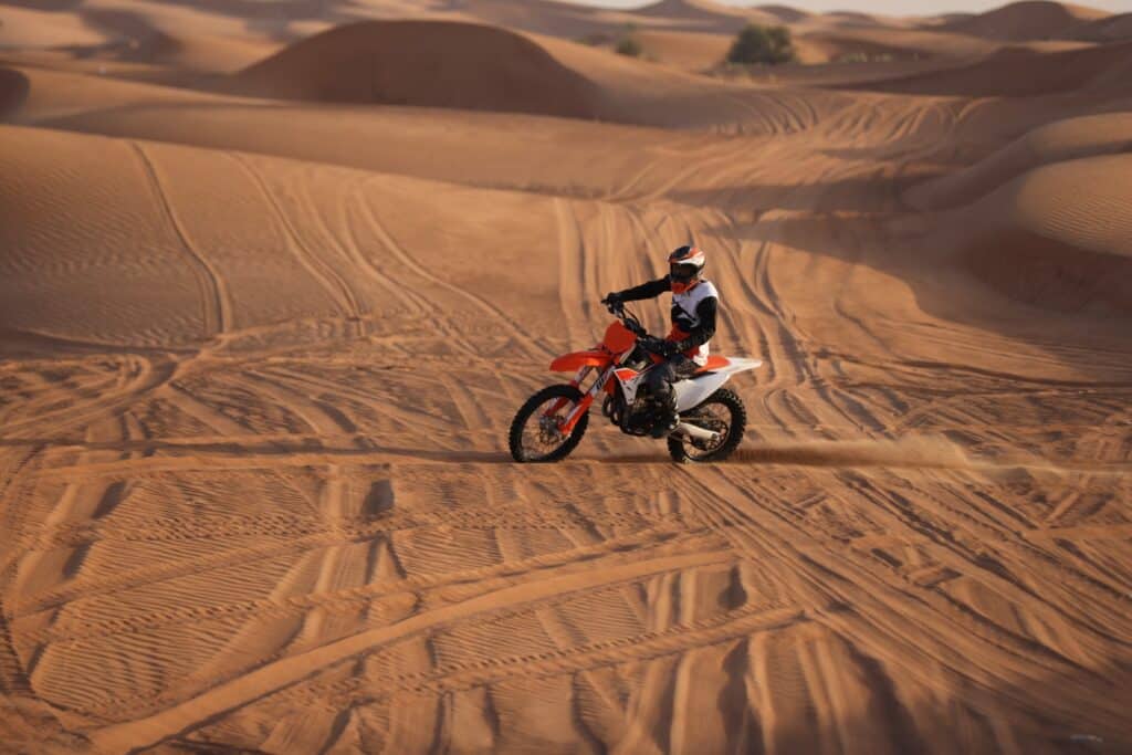 A man riding a dirt bike in the desert. A man riding orange color KTM 450CC in the desert