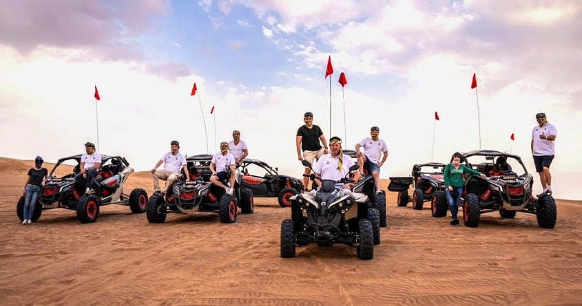 Group of men riding quads and posing for camera in the desert